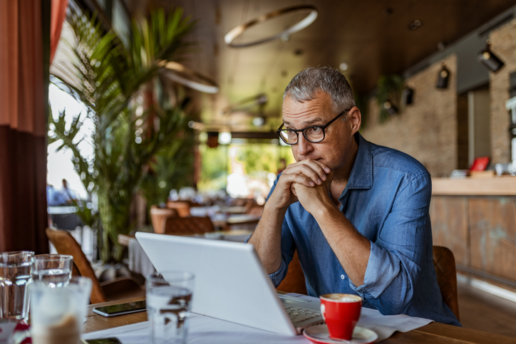 mężczyzna w okularach siedzi w kawiarni i pracuje na laptopie